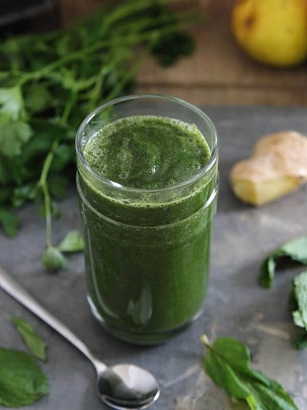Green detox smoothie in a glass next to a spoon.