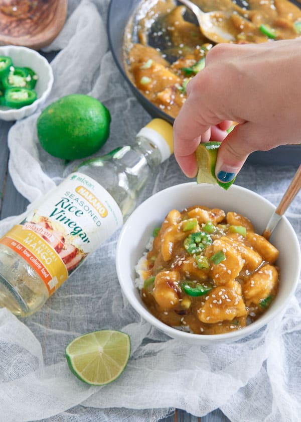 Squeezing a lime over mango chicken and rice in a white bowl.