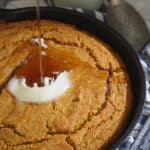 Vanilla pumpkin cornbread in a skillet with butter and maple syrup on top.