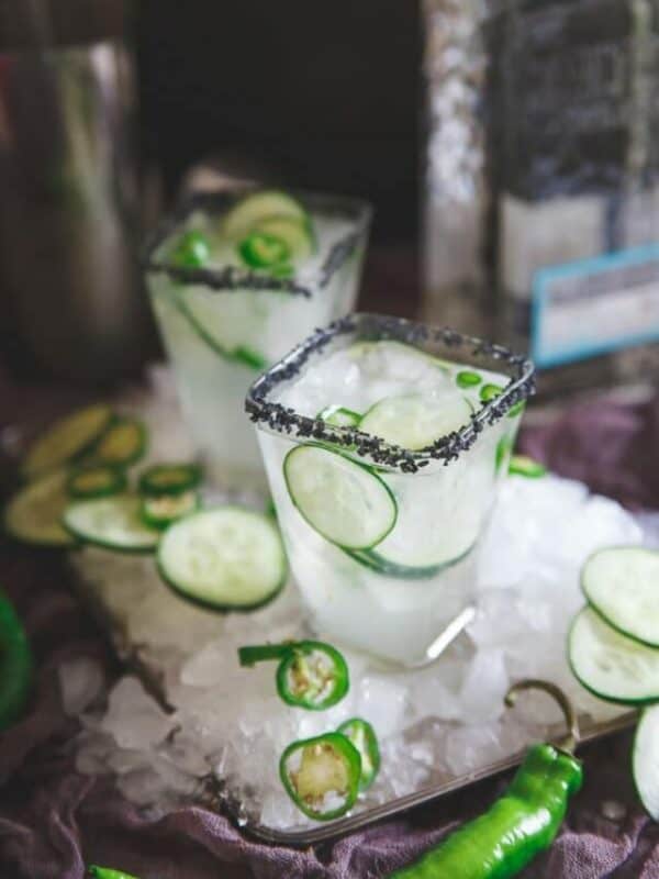 Two glasses of cucumber margarita with ice and peppers.