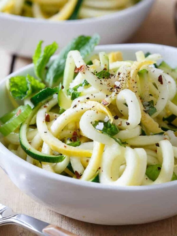 Zucchini and yellow squash noodles in a white bowl with mint garnish.