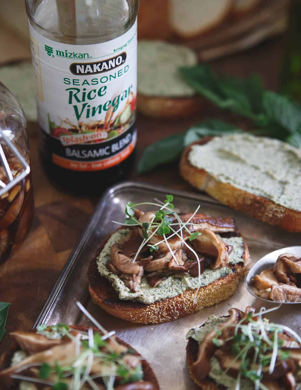 Balsamic Pickled Shiitake mushrooms are paired with a basil ricotta pesto spread for the perfect crostini bite.