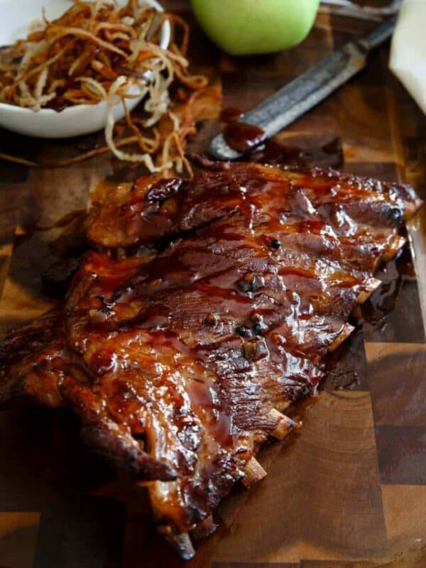 Glazed barbecue ribs served on a wooden board with a side of crispy onions.