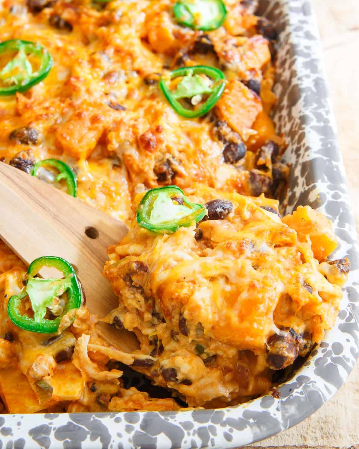 A wooden spoon scooping out some of the tortilla pumpkin casserole.