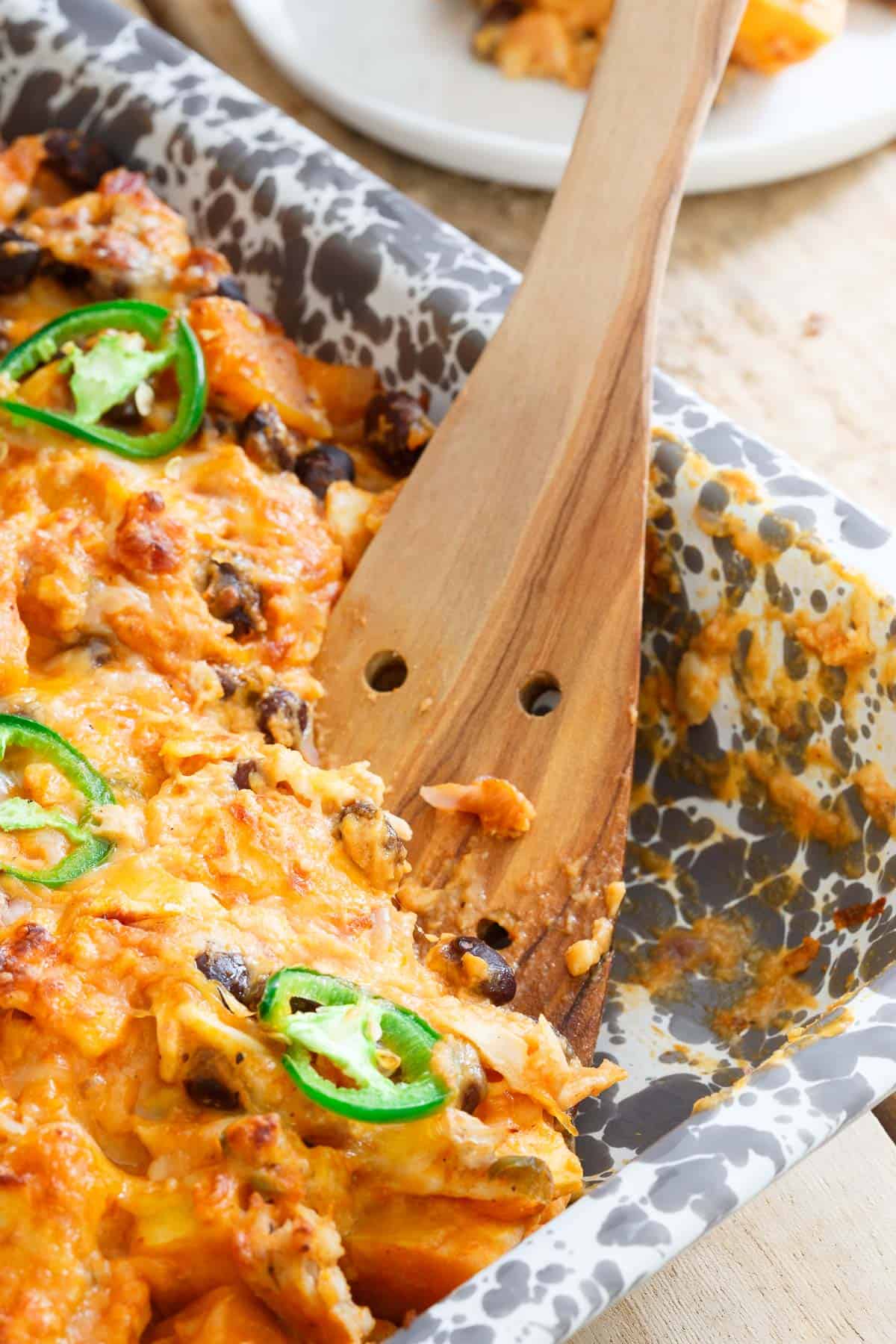 Cheesy pumpkin casserole in a baking dish with a wooden spoon and a scoop missing.