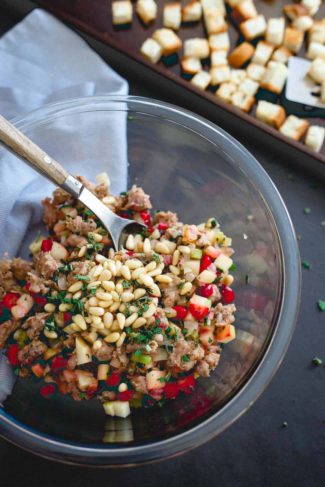 Mixing the ingredients for sausage stuffing muffins in a glass mixing bowl.