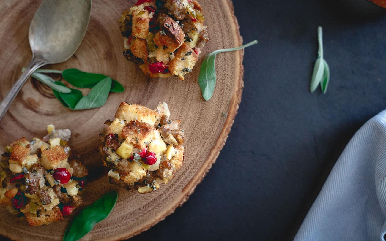 Three cranberry apple sausage muffins sitting on a wood board next to a spoon.