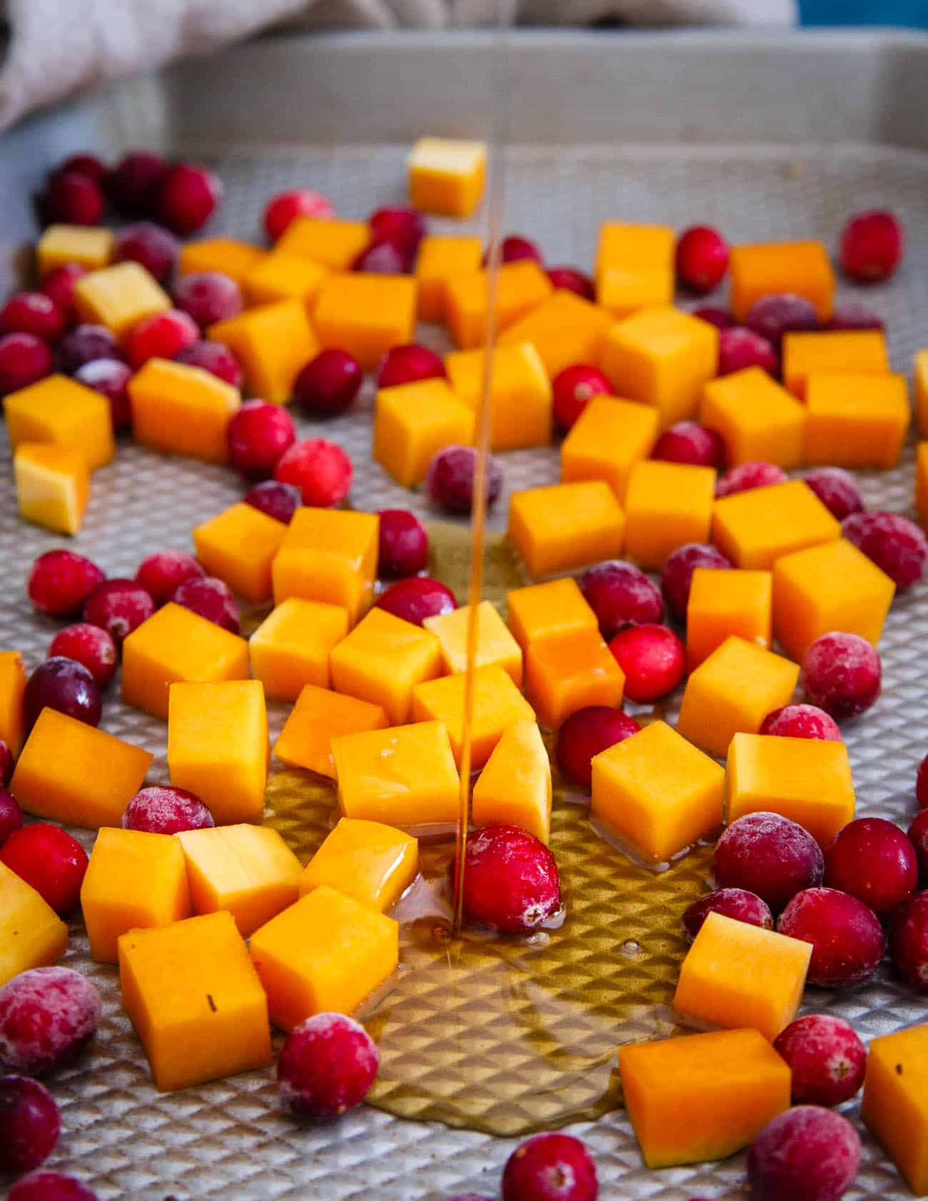 Adding maple syrup to cranberries and butternut squash on a baking sheet.