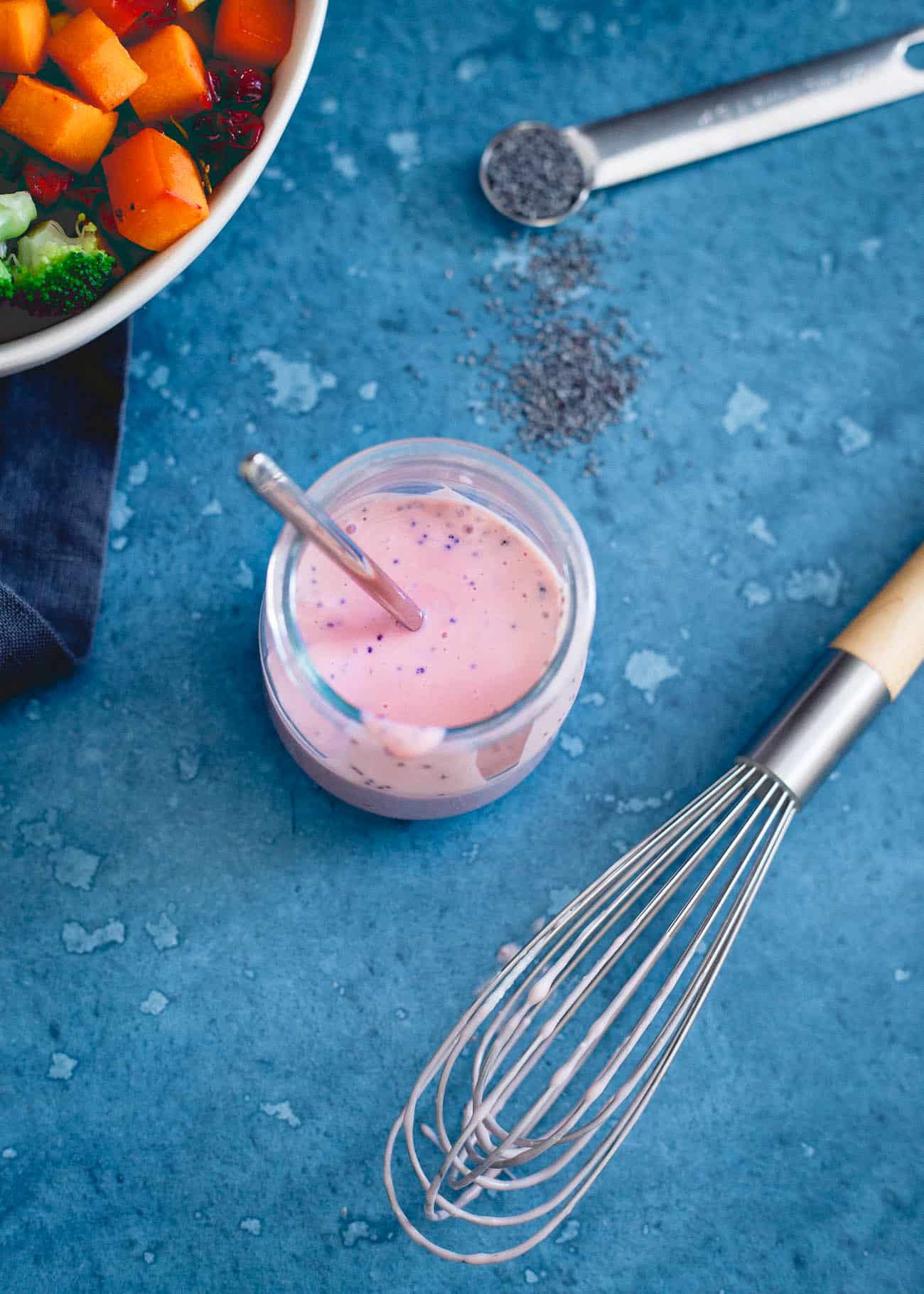 Homemade cranberry dressing in a jar next to a whisk.