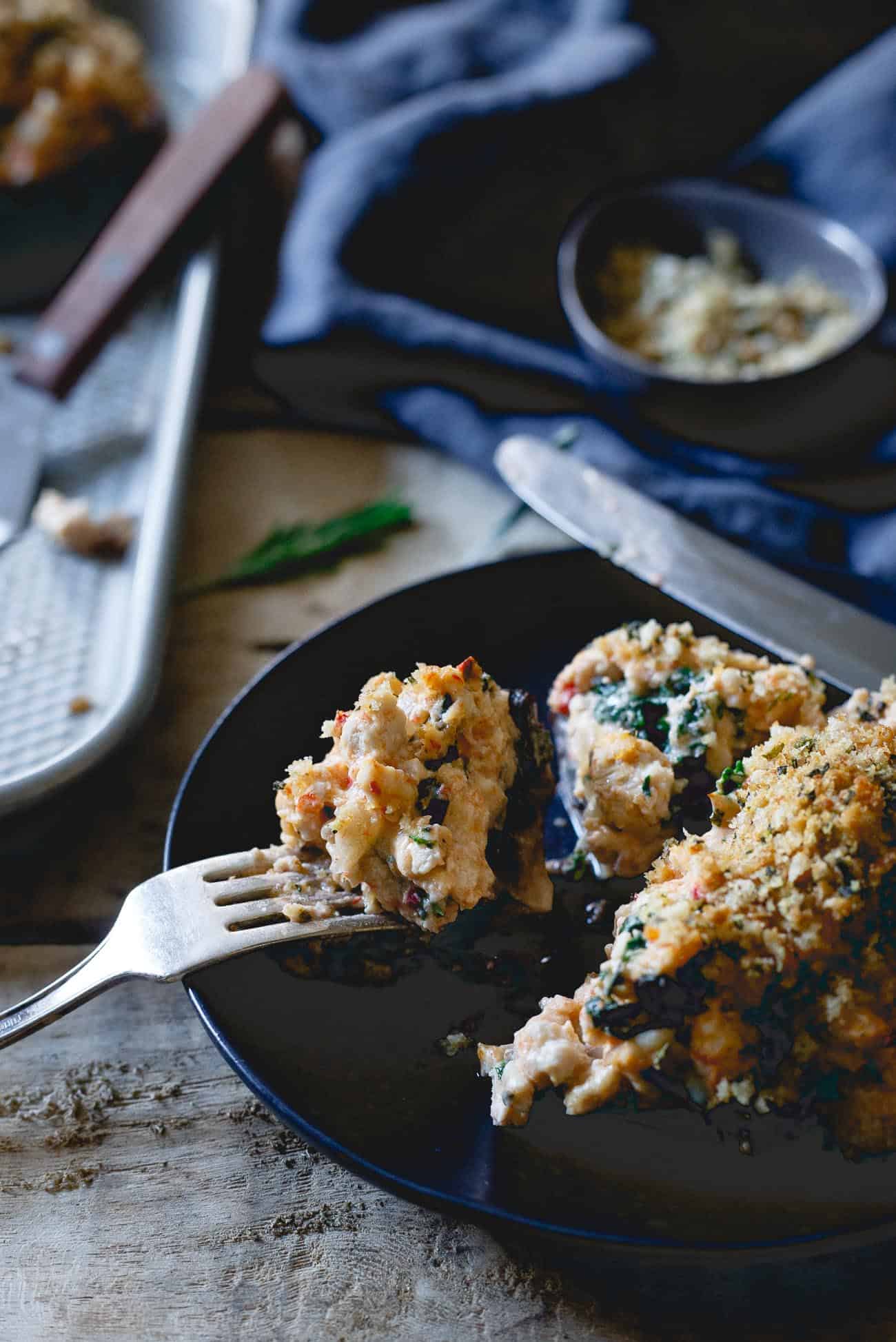 A fork stuck in a turkey stuffed mushroom on a black plate.