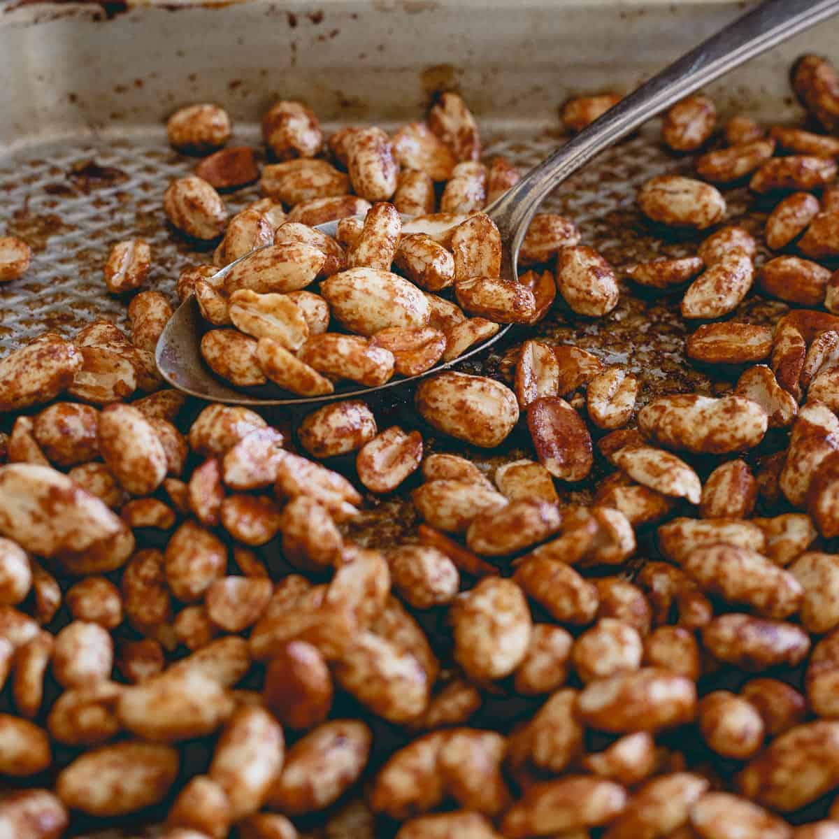 Molasses roasted peanuts on a pan with a spoon.