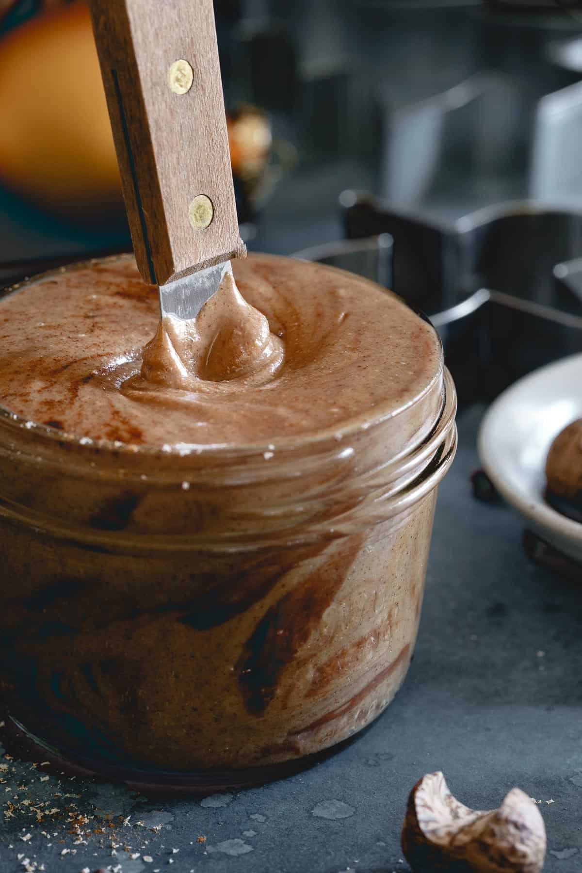 Homemade gingerbread nut butter in a jar with a spatula sticking out.