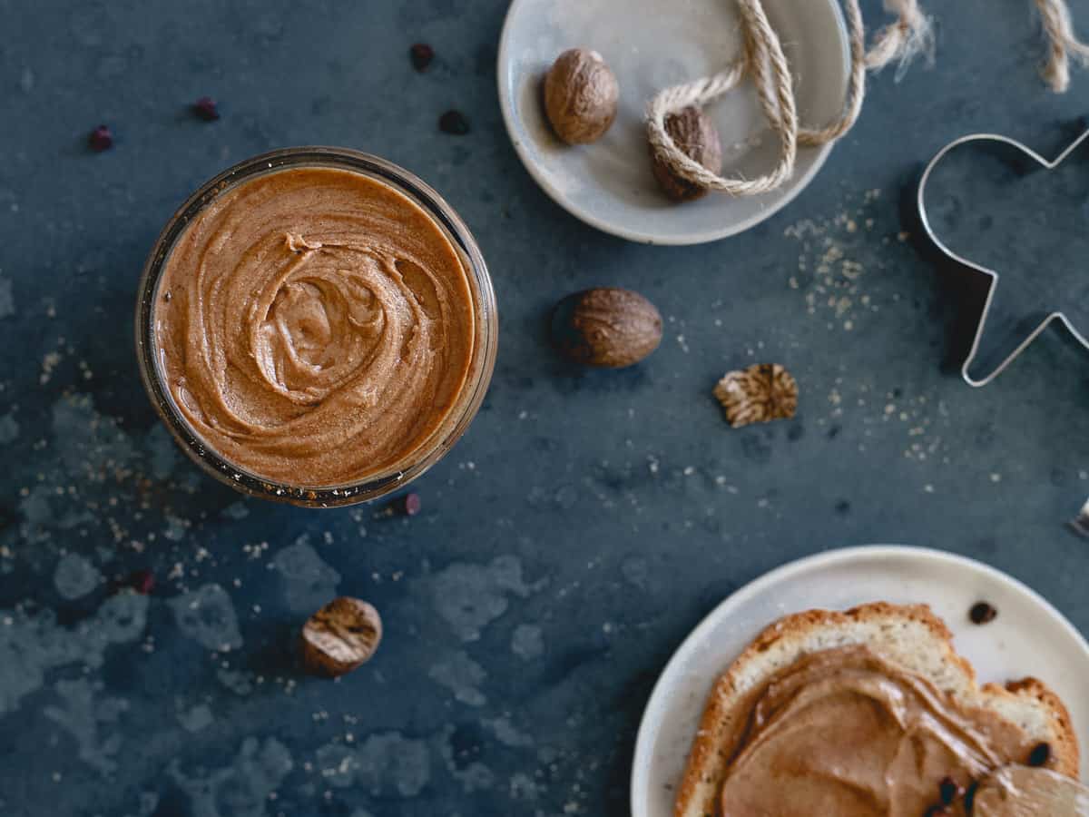 Top view of gingerbread peanut butter in a glass jar next to nuts and a cookie cutter.