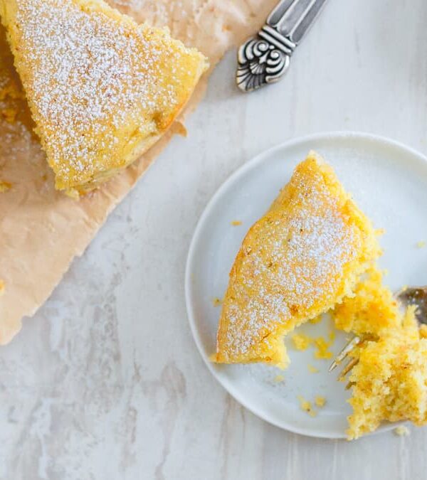 Orange glazed cardamom cake on a white plate with a fork.