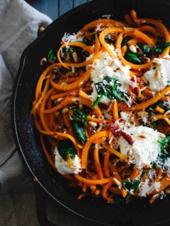 These garlicky butternut squash noodles are tossed with wilted spinach, sun-dried tomatoes, toasted pine nuts and dollops of fresh ricotta and parmesan for a wintry, one-pan, comforting vegetarian meal. 