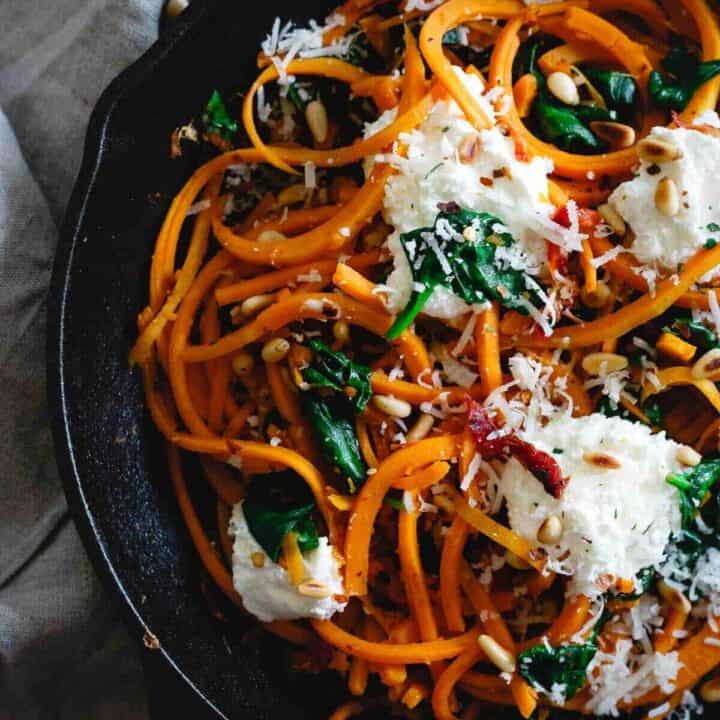These garlicky butternut squash noodles are tossed with wilted spinach, sun-dried tomatoes, toasted pine nuts and dollops of fresh ricotta and parmesan for a wintry, one-pan, comforting vegetarian meal.
