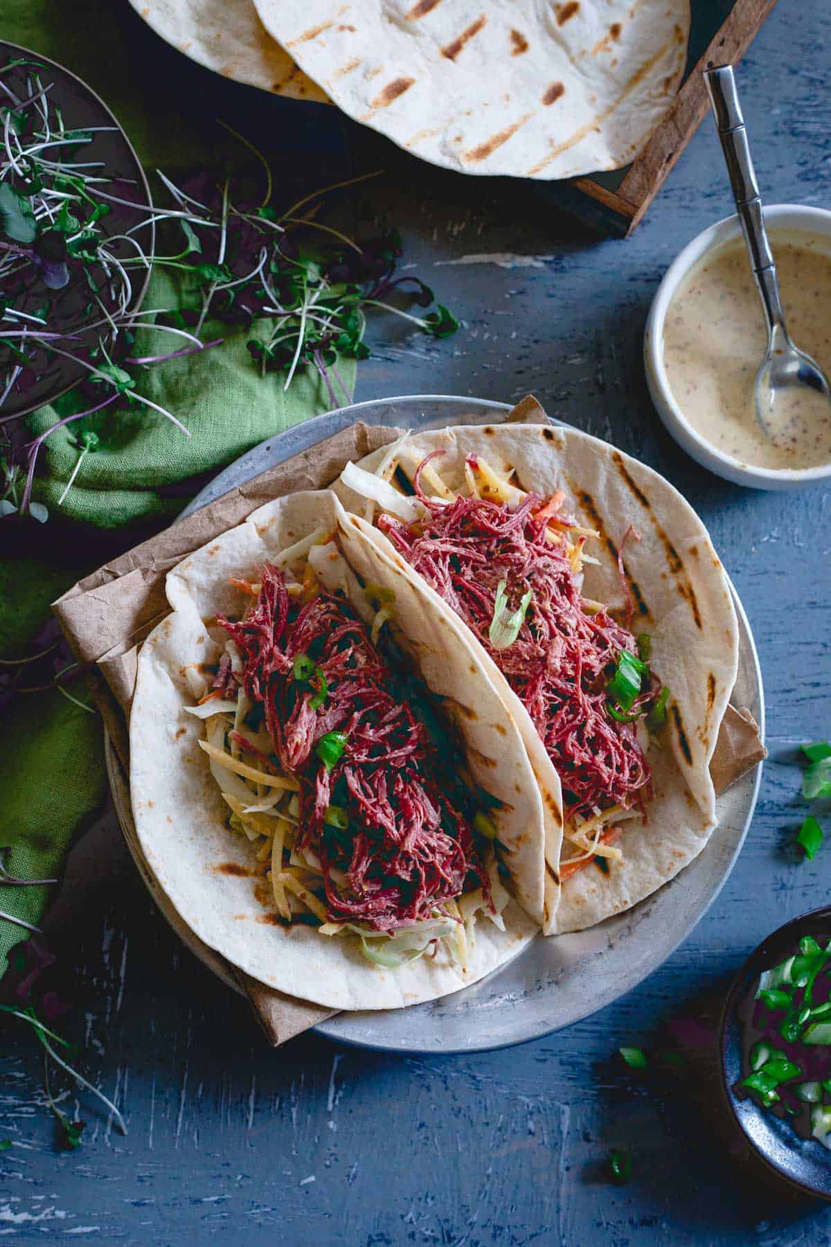 Corned beef tacos are served with a carrot cabbage slaw both tossed in a creamy spicy mustard sauce.