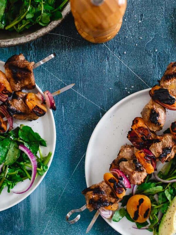 Two plates with meat skewers and salad on them.