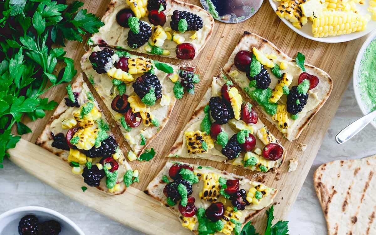 This hummus flatbread is a pre-dinner snack bursting with summer flavors from grilled corn to berries, cherries and fresh parsley pesto.