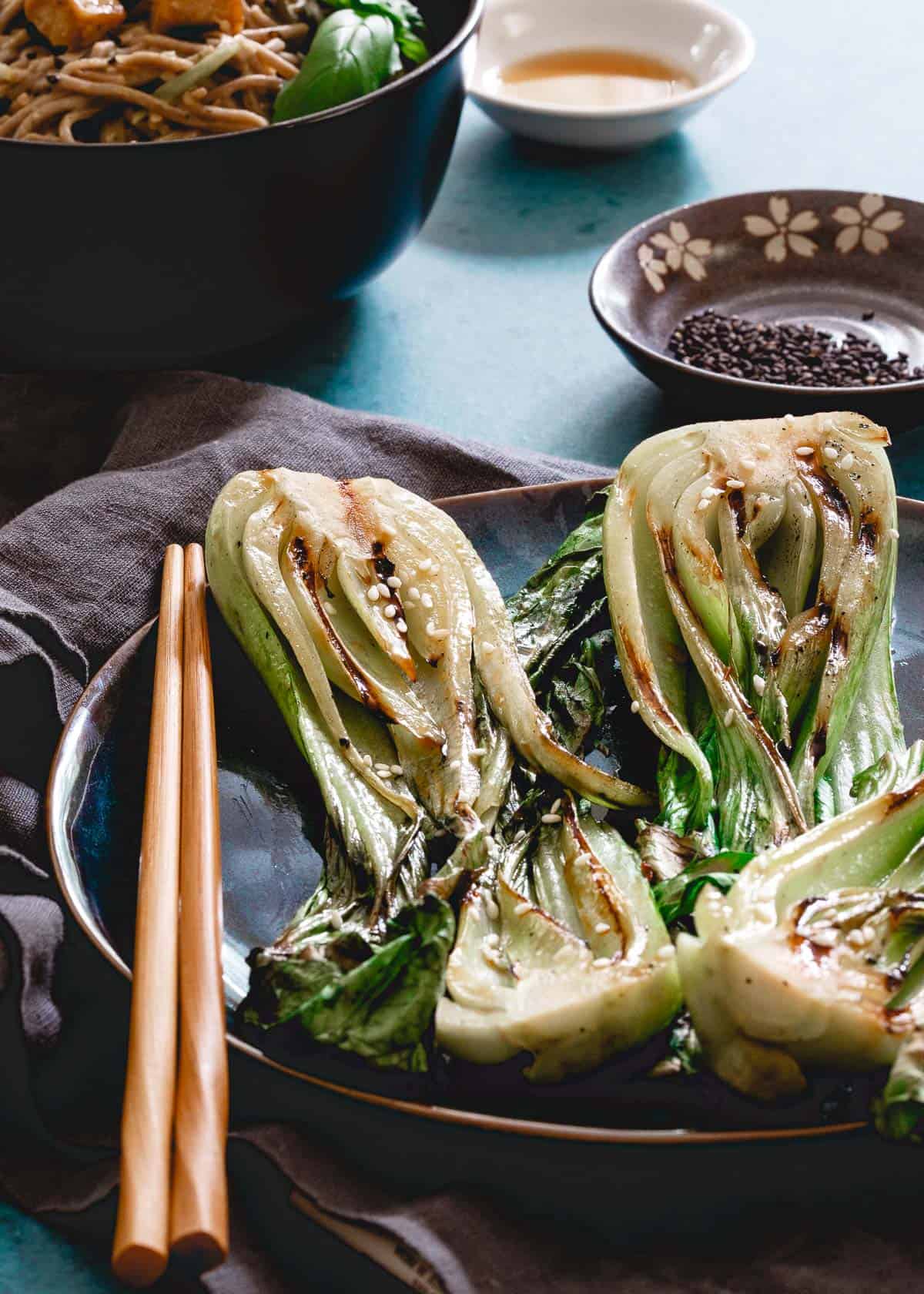 Asian inspired grilled baby bok choy on a plate next to chop sticks.