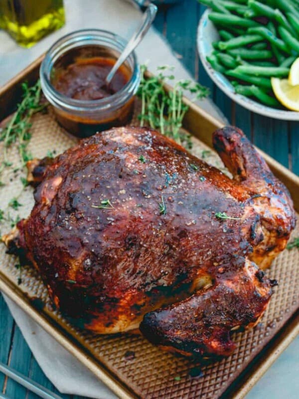 A roasted chicken on a baking sheet with sauce and green beans.