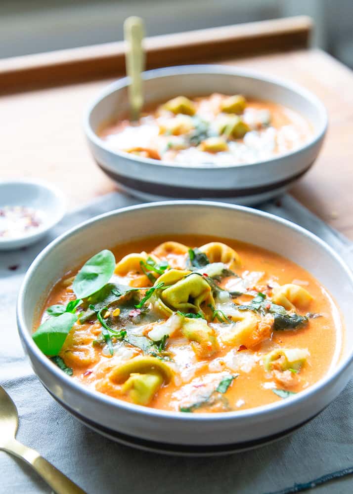 Pressure cooker tortellini soup in two bowls topped with fresh basil.