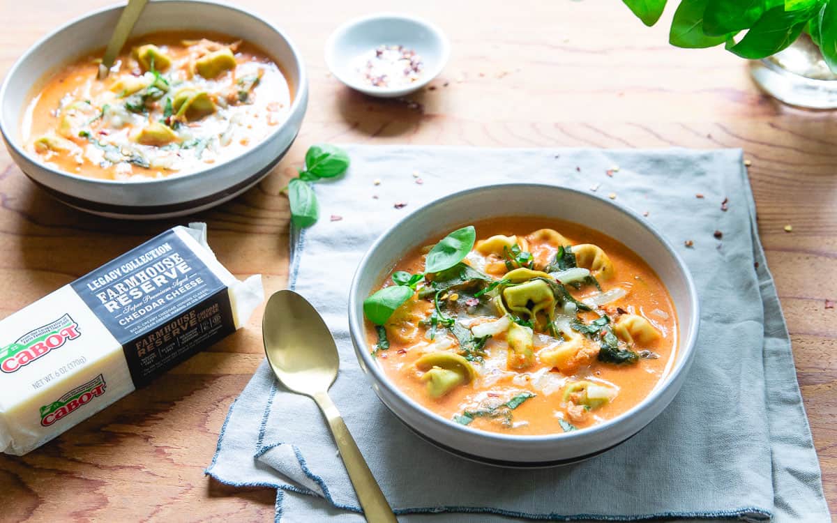 Two bowls of creamy tortellini soup made in the instant pot next to cheese and a gold spoon.