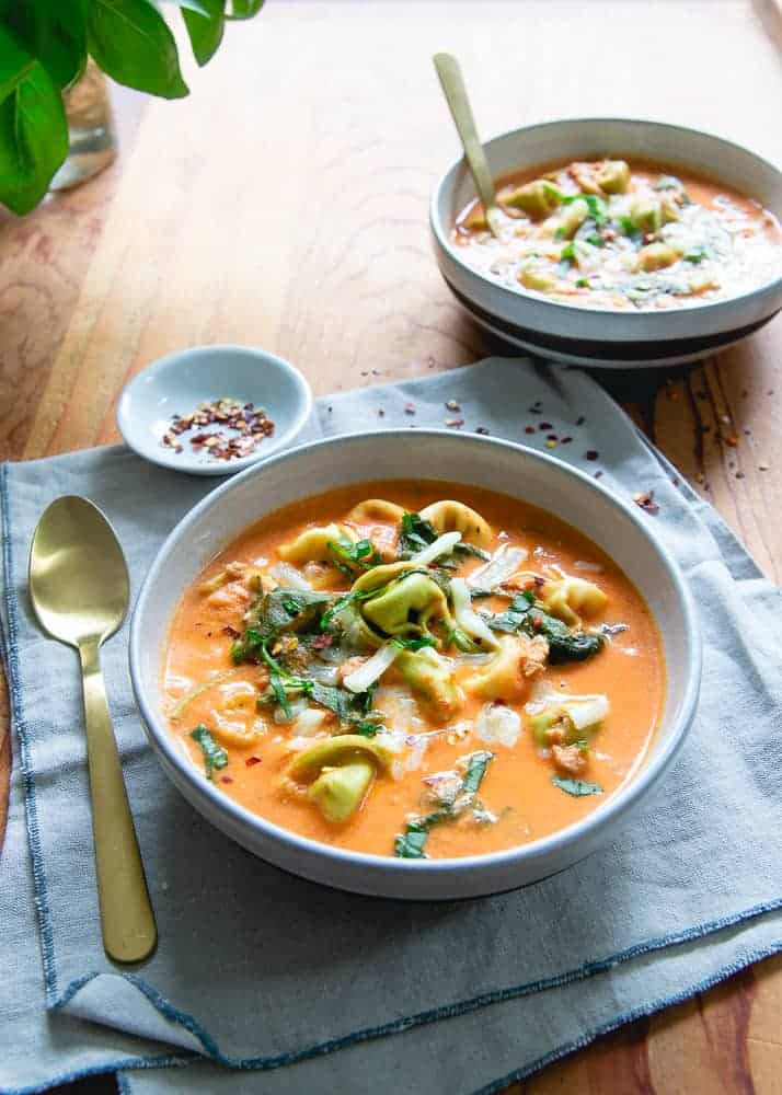 Instant Pot creamy tomato tortellini soup in a bowl on a napkin with a gold spoon on the side.