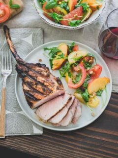 Harissa rubbed grilled pork chops are a simple, spicy summer meal perfectly paired with a ripe peach and tomato salad and glass of sweet red wine.