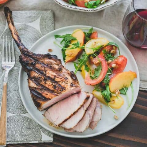 Harissa rubbed grilled pork chops are a simple, spicy summer meal perfectly paired with a ripe peach and tomato salad and glass of sweet red wine.