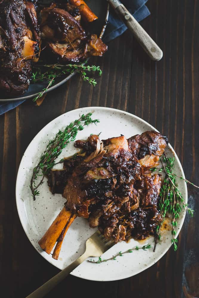 Top view of braised lamb shanks made without wine on a white plate with fresh herbs and a gold fork.