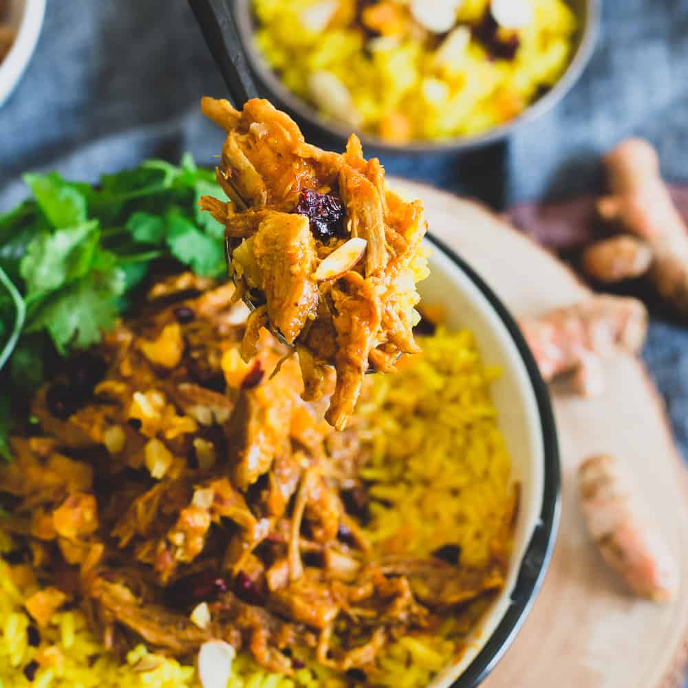 Instant Pot coconut pork shoulder is shredded and served over a bed of aromatic rice with dried fruit and nuts.