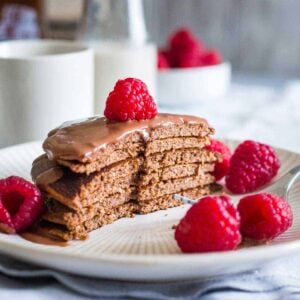 Chocolate protein pancakes with chocolate sauce and raspberries on a plate.