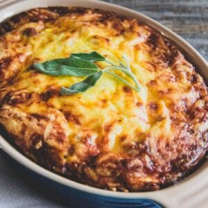 Cheesy potato breakfast casserole in a baking dish topped with sage leaves.