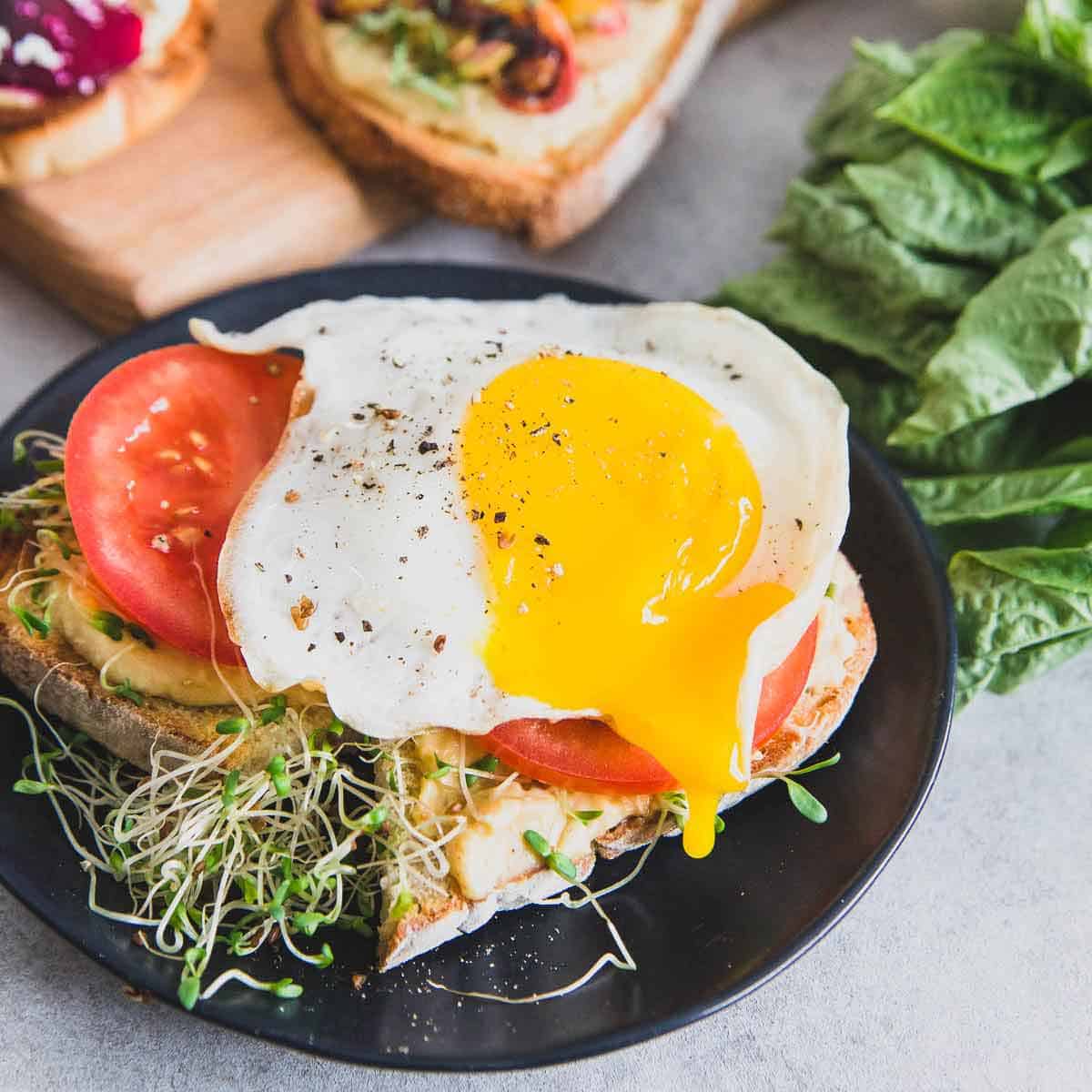 A runny fried egg tops sourdough hummus toast with fresh tomato slices along with a delicious beet smoothie recipe.