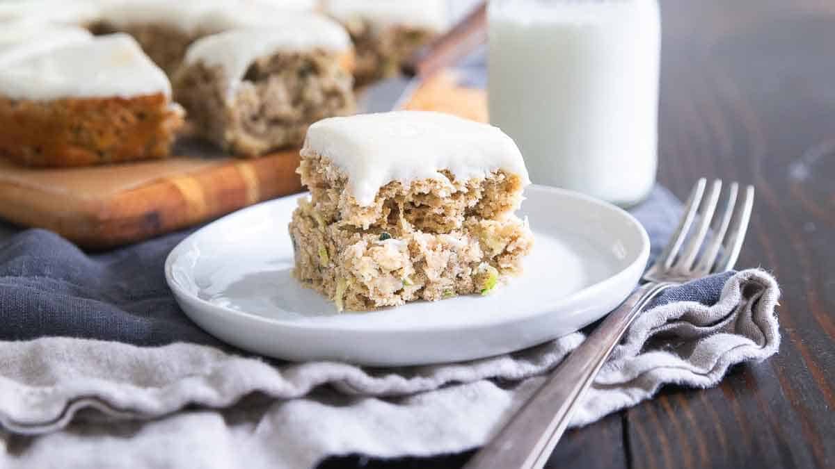 Zucchini bars with cream cheese frosting on a plate with a fork on the side.