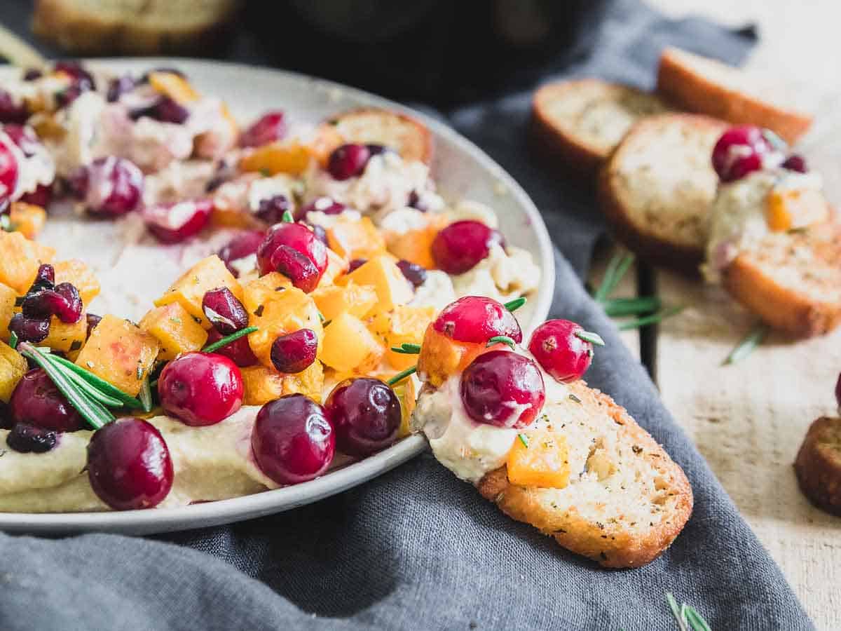 Rosemary roasted butternut squash, fresh cranberries and bright pomegranate arils top creamy hummus for a fun holiday twist on this classic appetizer.