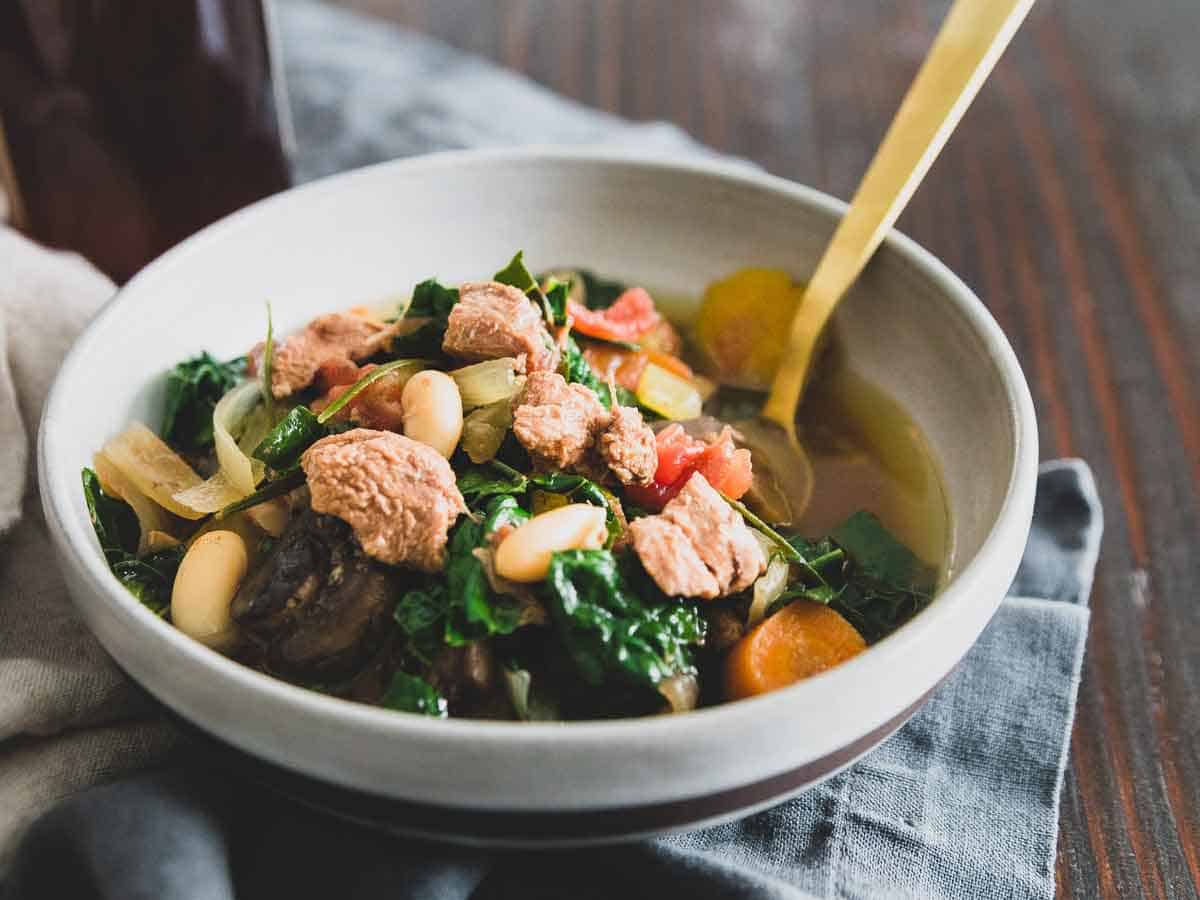 A lamb stew slow cooker recipe with hearty white beans, mushrooms, kale, tomatoes and carrots flavored with fresh rosemary.