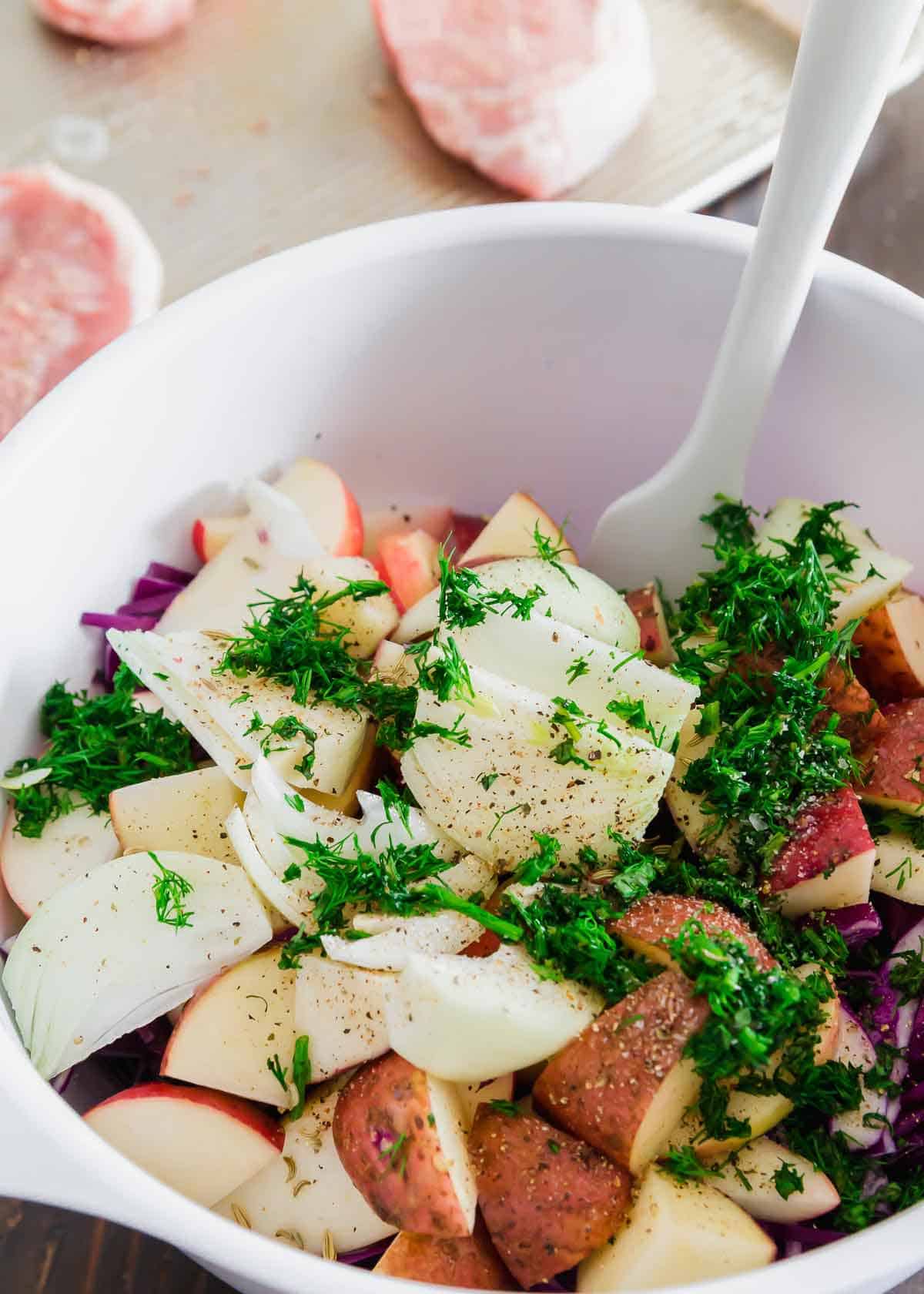 Purple cabbage, red potatoes and apples are tossed with fresh herbs and spices to bake alongside boneless pork chops in this sheet pan meal.