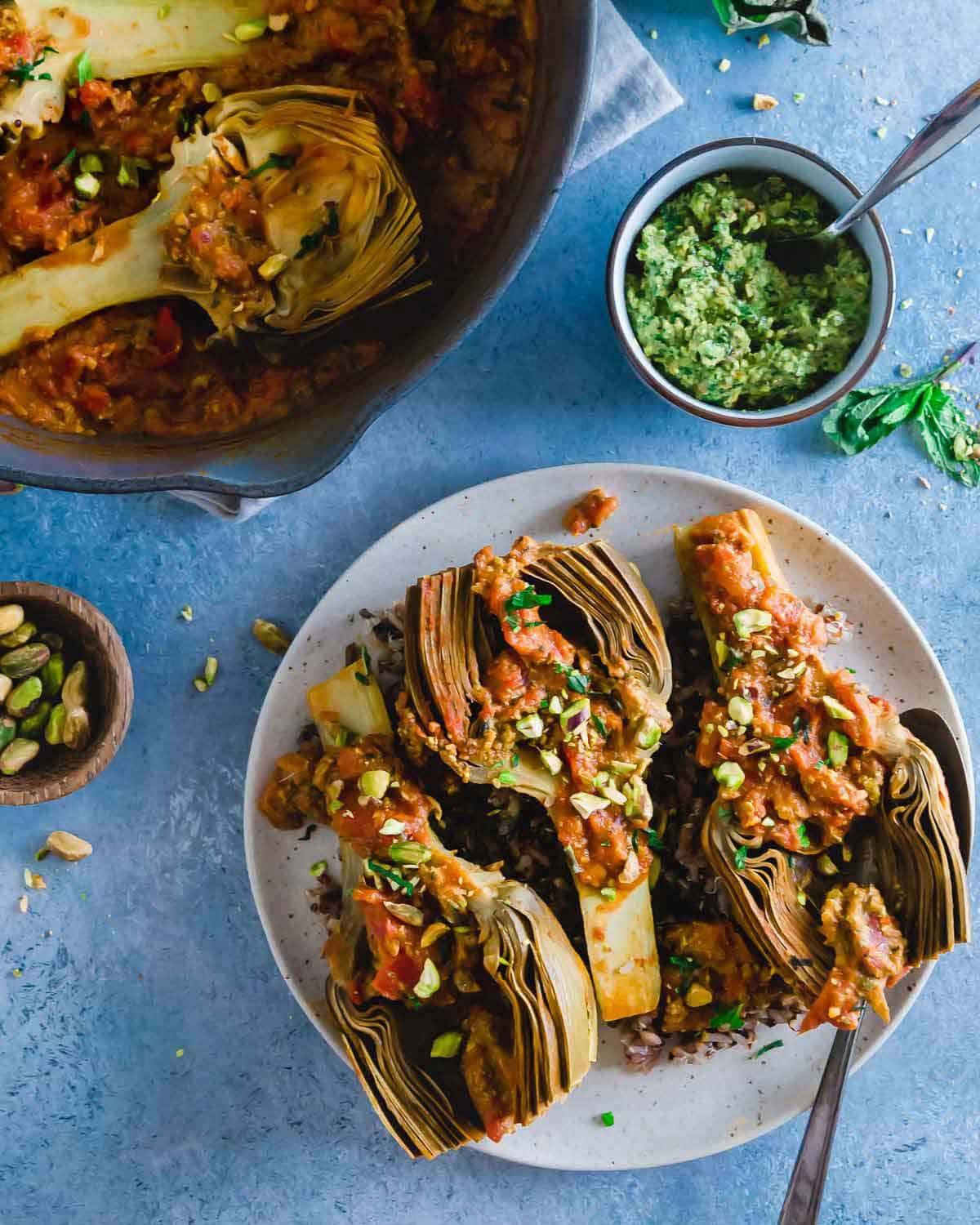 Braised artichokes cooked with tomatoes until fork tender and served with pistachio pesto are an absolutely delicious vegetarian side dish.