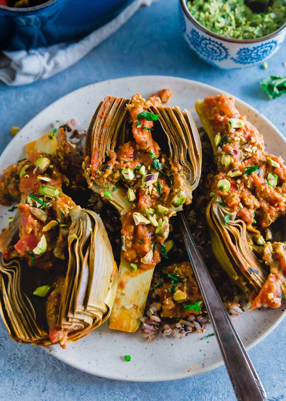 Braising artichokes results in the perfect fork tender vegetarian side dish. These cook down with whole peeled tomatoes and white wine and are served with a bright pistachio pesto.