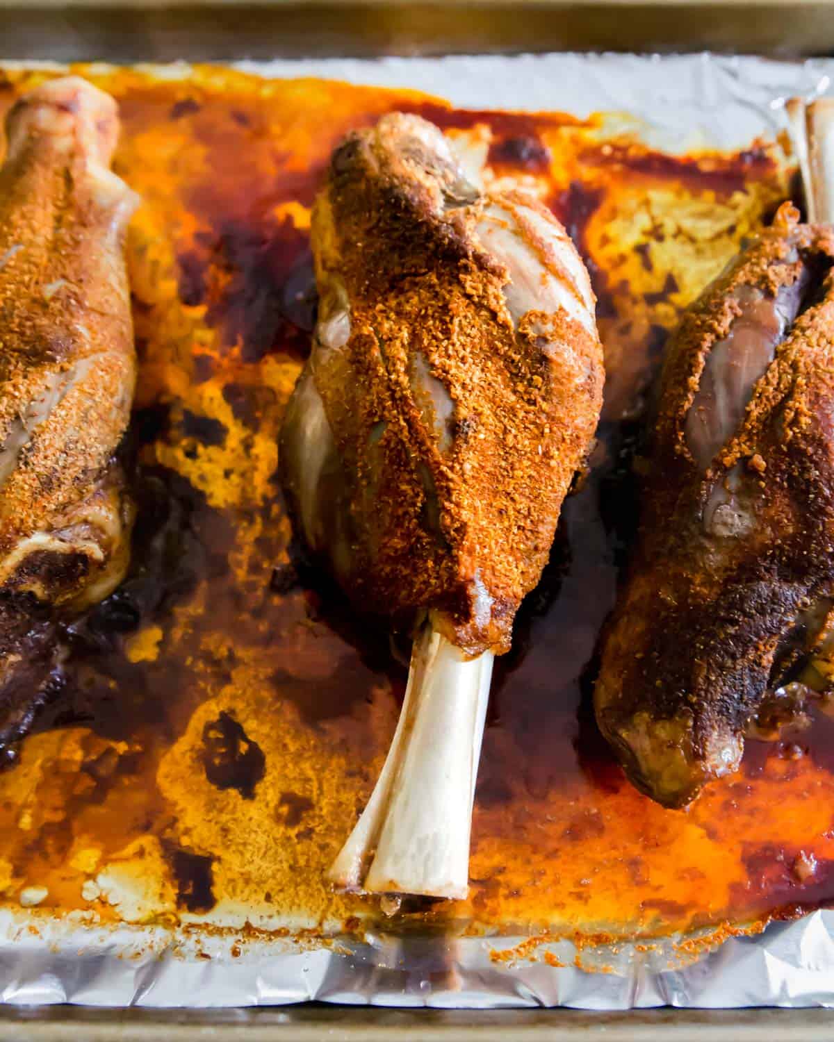 After baking, these BBQ lamb shanks are slathered in BBQ sauce and then finished on the grill.