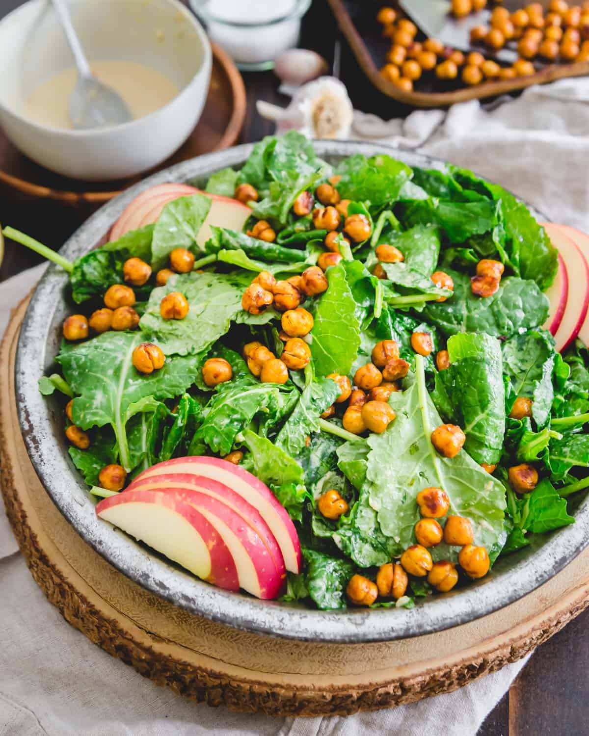 Ein sättigender und nahrhafter Grünkohlsalat auf pflanzlicher Basis mit gerösteten Kichererbsen, Äpfeln und einem cremigen Tahini-Dressing.