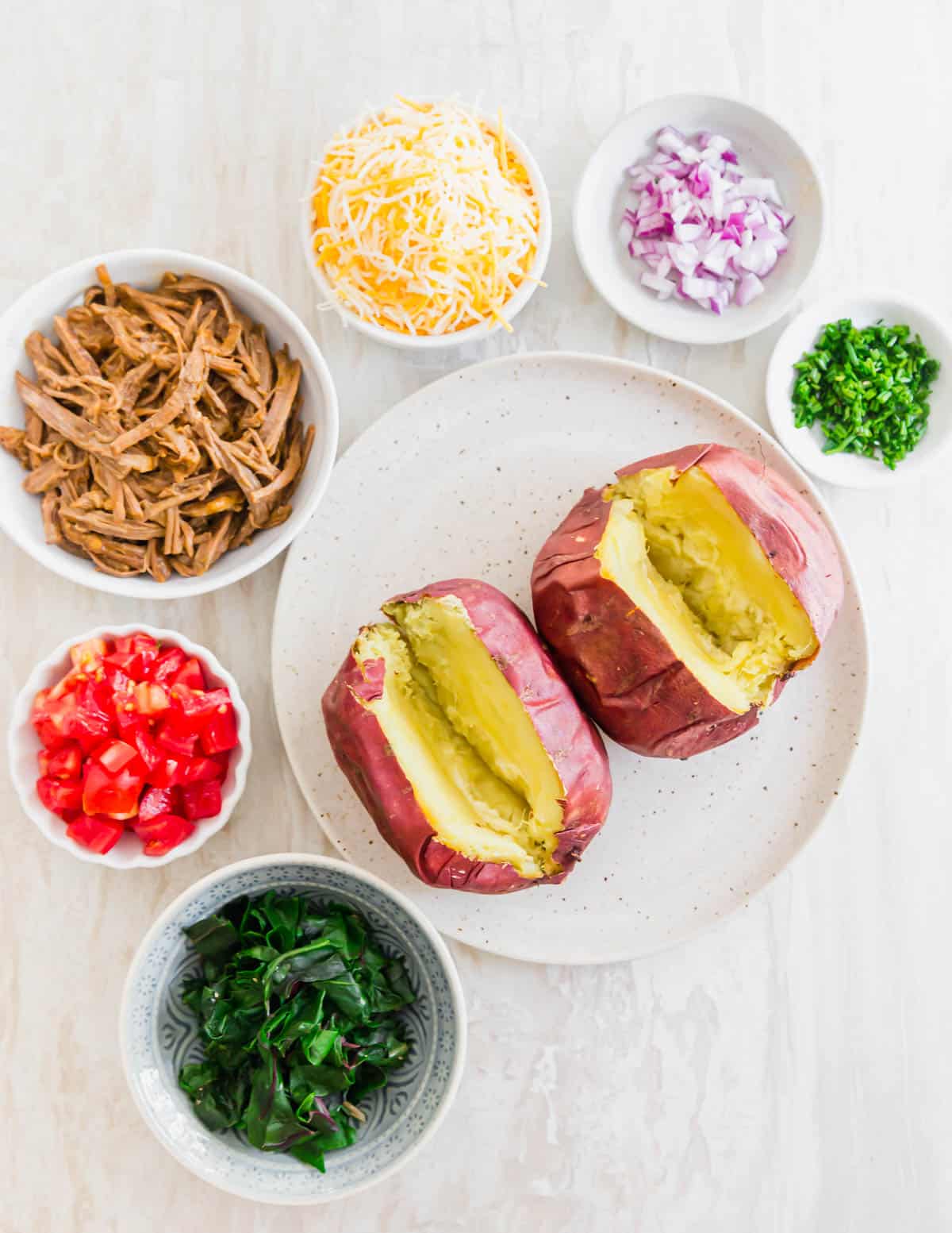 Ingredients needed to make brisket baked potatoes - leftover cooked and shredded beef brisket, cheese, red onion, tomato, greens and chives.