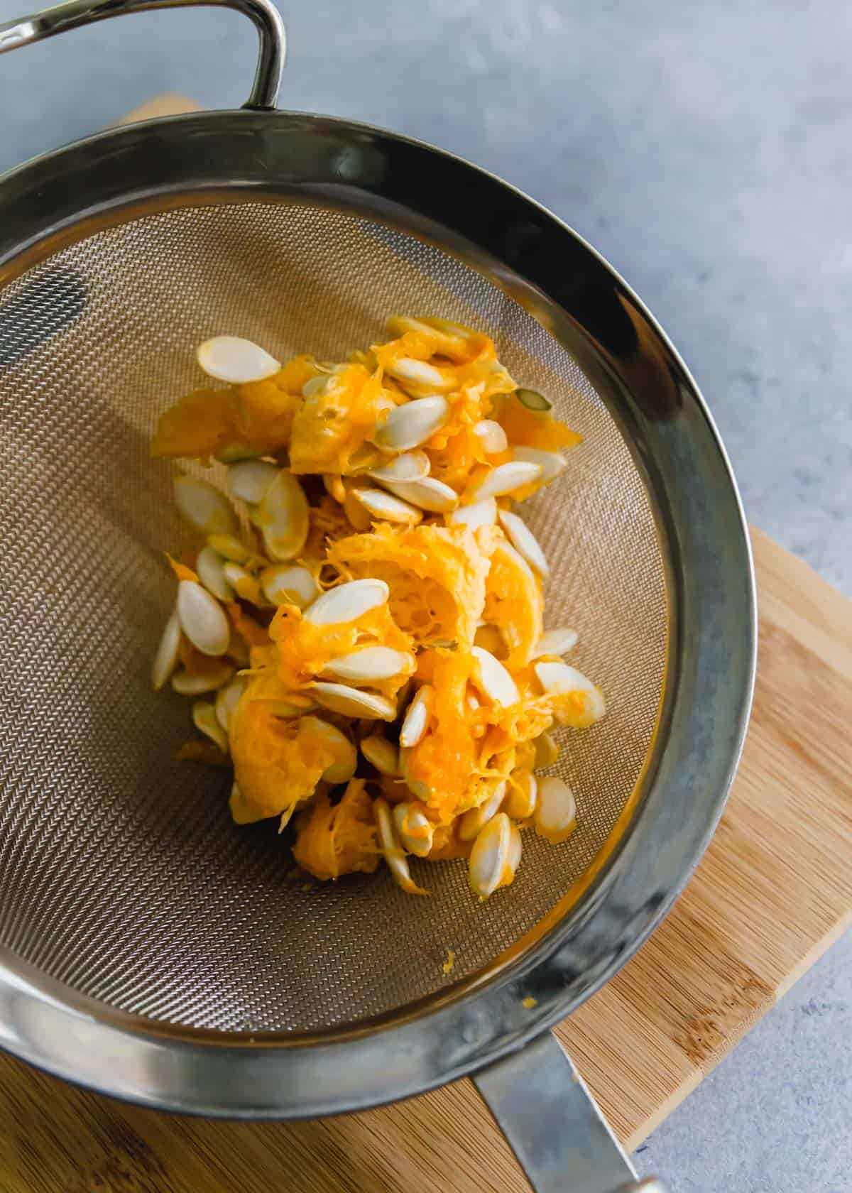 squash seeds before cleaning with pulp still attached in a colander.