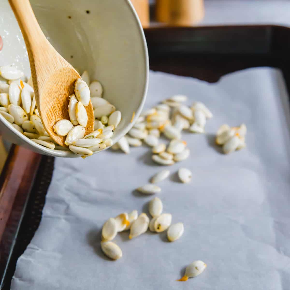 Spreading out seasoned squash seeds onto a parchment lined baking sheet before roasting