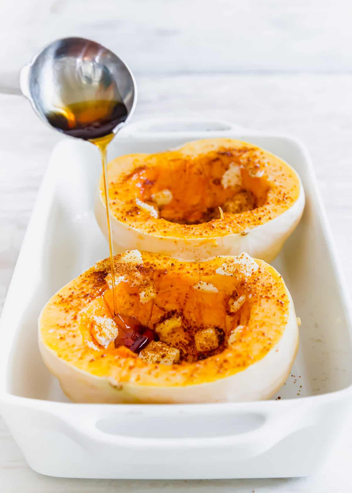 white acorn squash with butter, sugar and maple syrup before baking in a baking dish