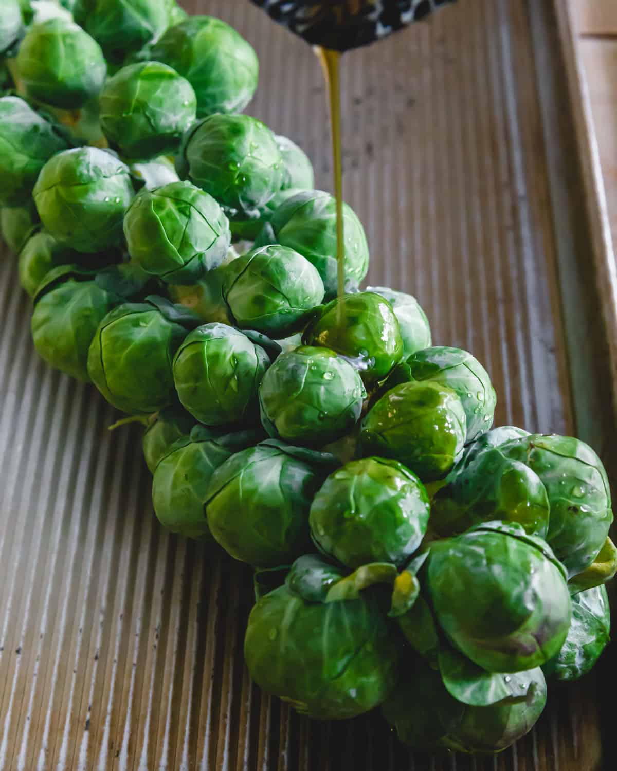 maple balsamic glaze being poured over Brussels sprout stalk on baking sheet.