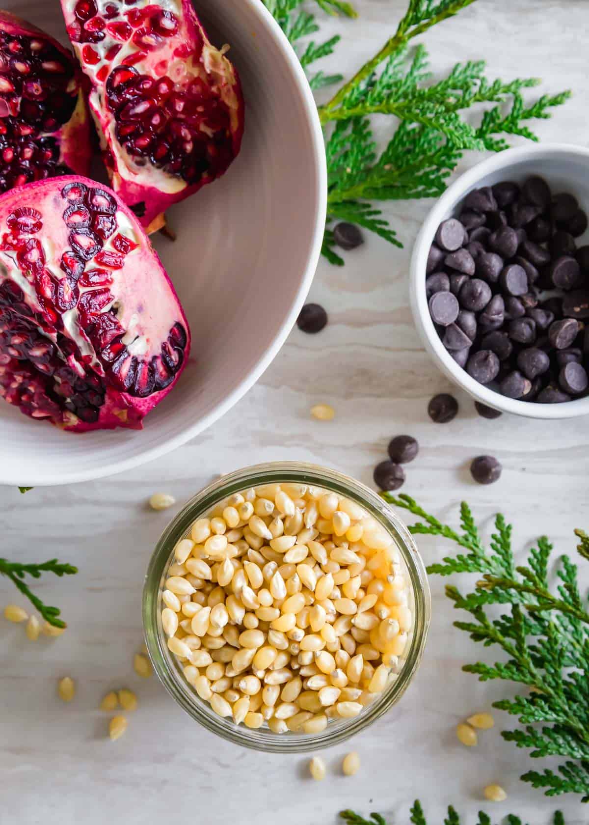 Ingredients to make pomegranate popcorn include popping corn kernels, pomegranate arils and dark chocolate chips.