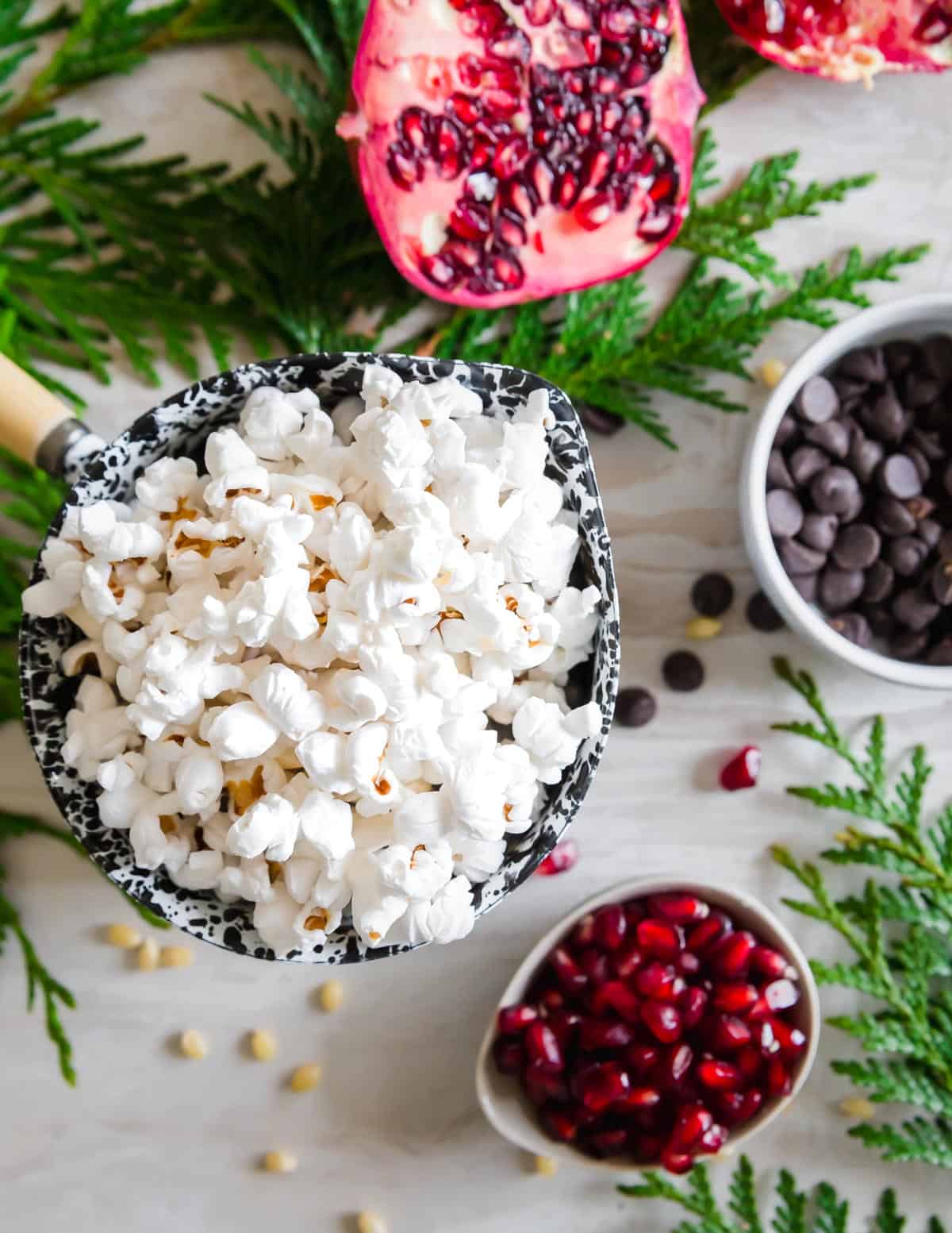 Freshly popped corn in coconut oil is tossed with bright and festive pomegranate, dark chocolate chips and a dusting of lemon zest.